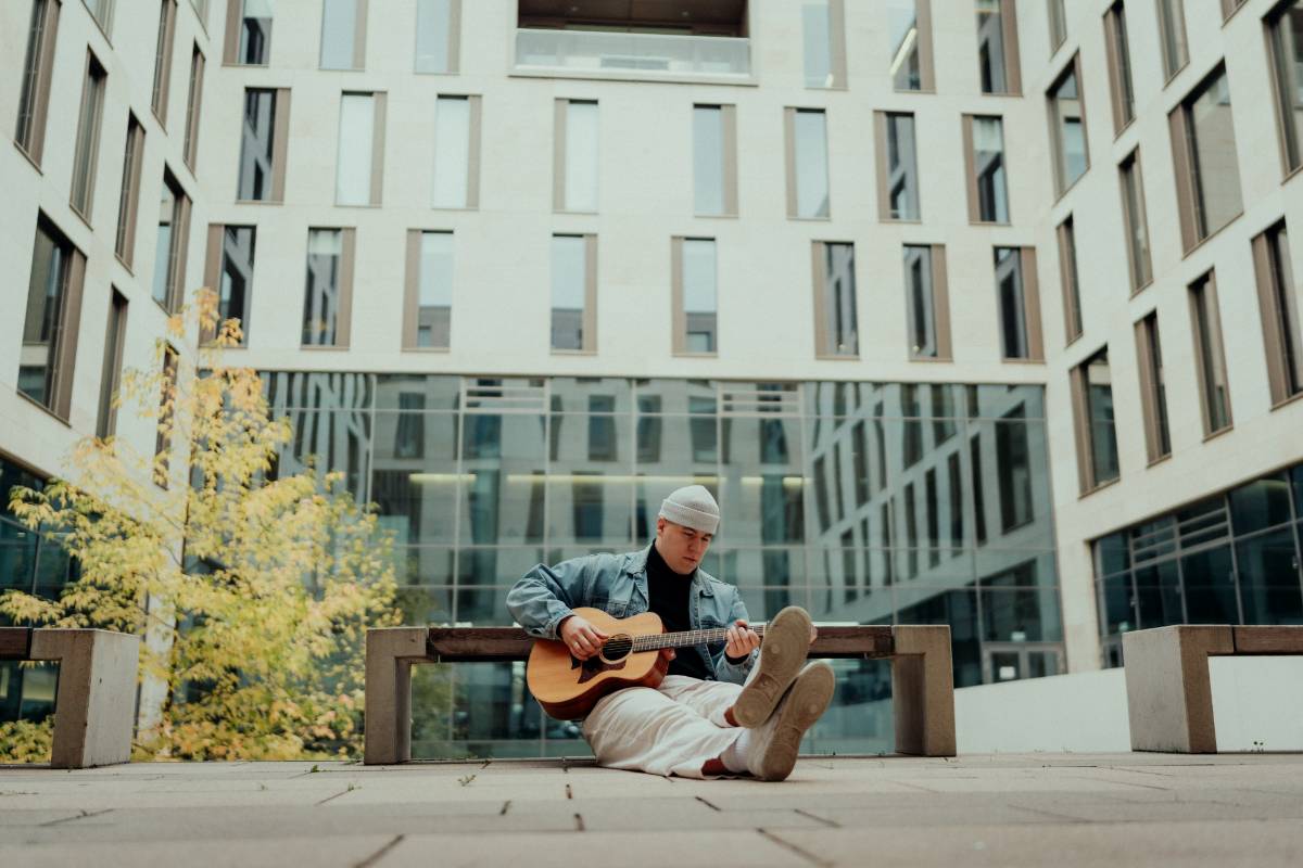 Der Musiker Jonny vom Dahl sitzt auf dem Boden vor einem Gebäude und spielt Gitarre