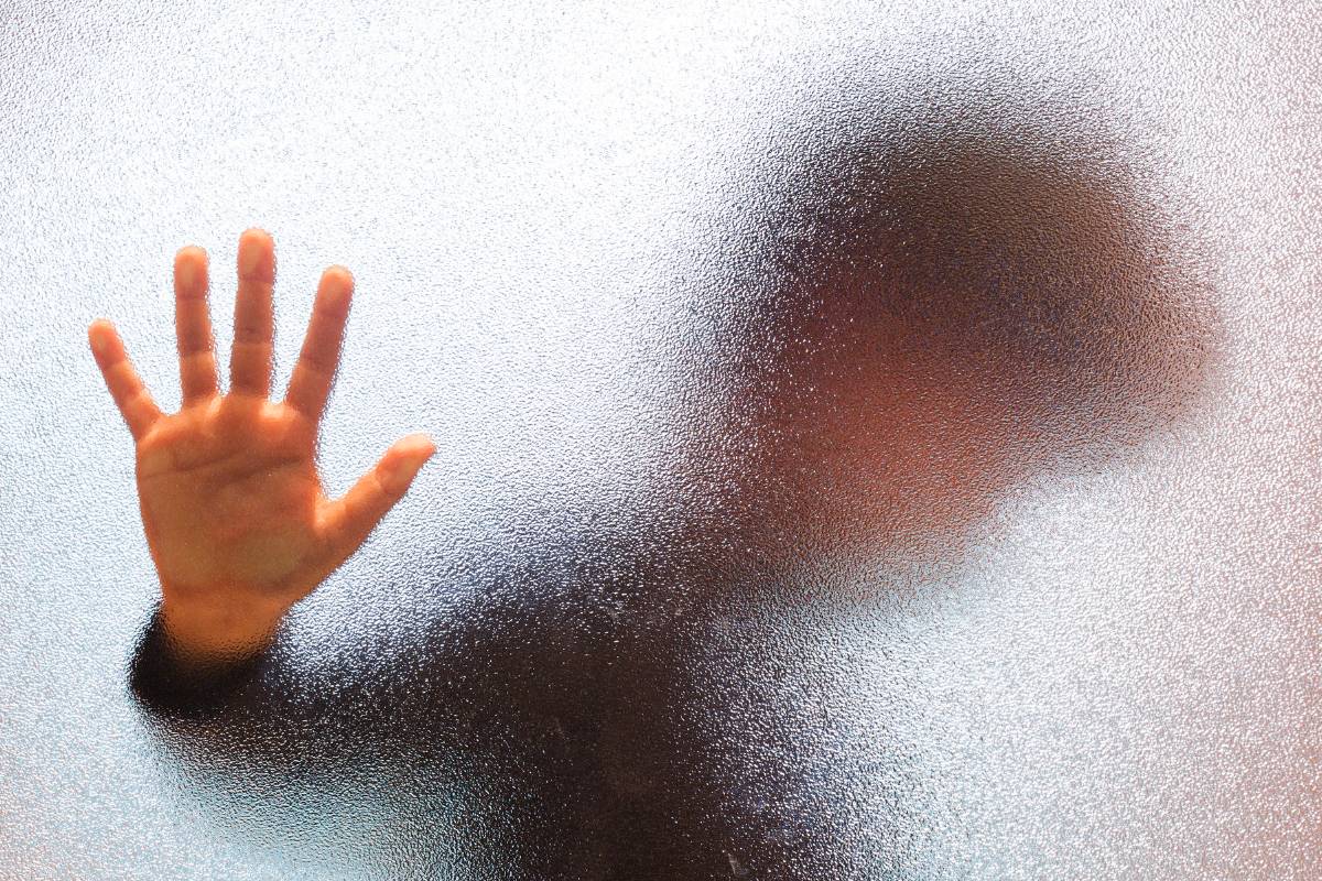 Junge hinter einer Glastür mit abwehrender hand