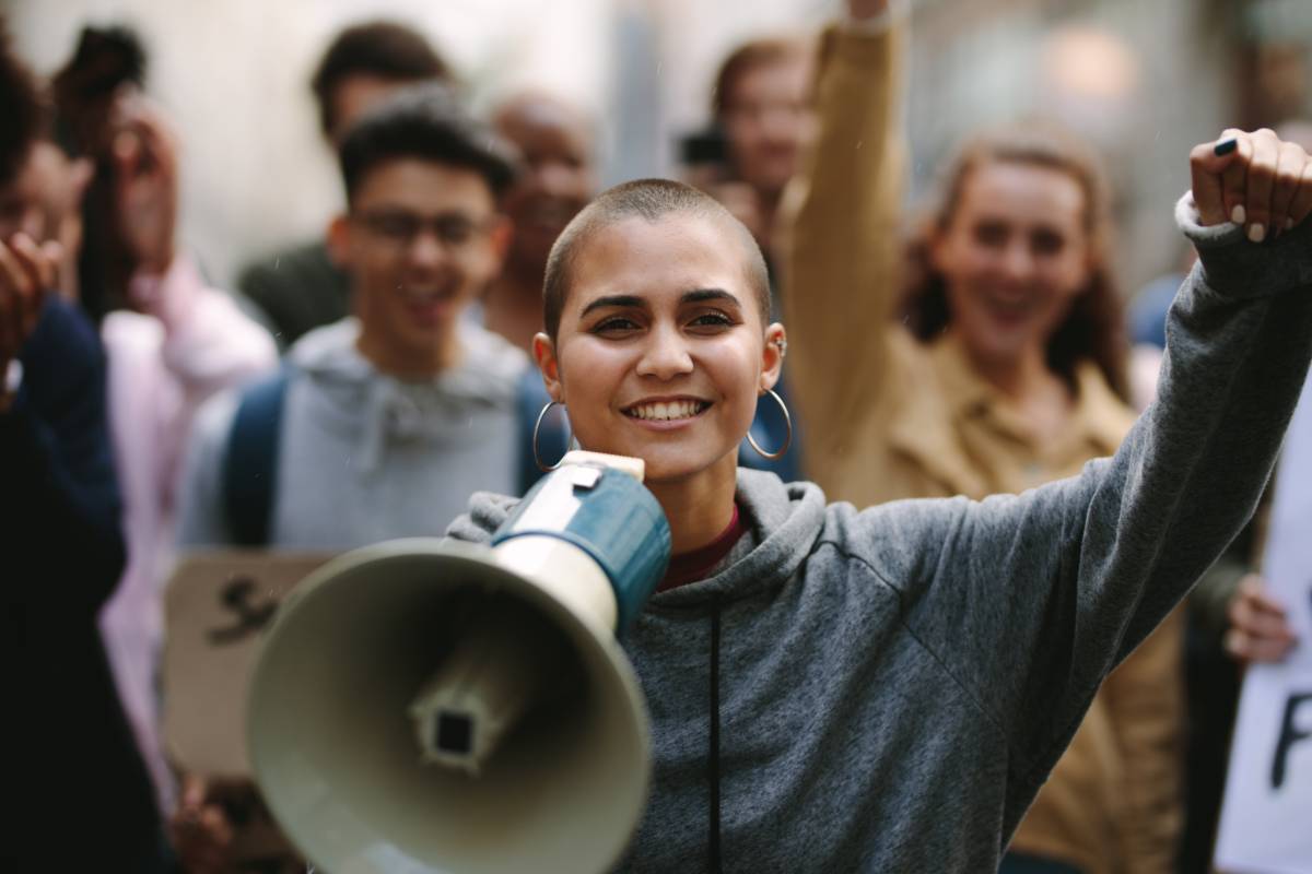Jugendliche protestieren, eine junge Frau steht mit einem Megafon im Mittelpunkt des Bildes