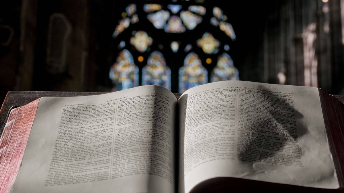 Eine Bibel liegt auf einer Kanzel. Im Hintergrund sieht man ein Kirchenfenster.