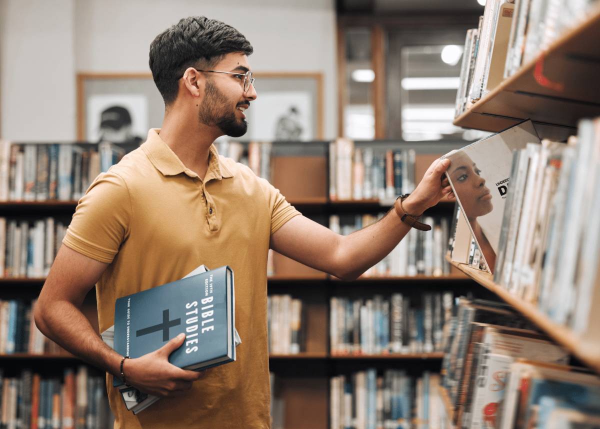 Mann in Bibliothek hält Bibel in der Hand